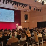 Panoramic view of FH Joanneum Audimax Conference Room, plenty of audience. A big screen shows the Diverse Courses Final Conference welcome message.