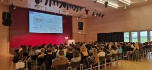Panoramic view of FH Joanneum Audimax Conference Room, plenty of audience. A big screen shows the Diverse Courses Final Conference welcome message.